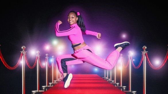 Image of an elegant dancer gracefully positioned on a luxurious red carpet, illuminated by radiant spotlights from above.